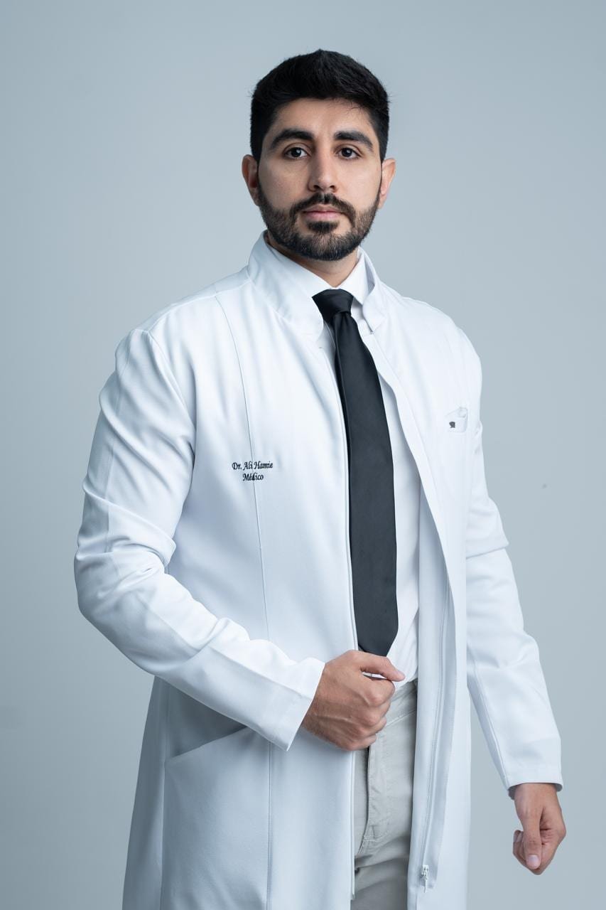 Dr. Ali Hamie de jaleco branco, com o nome e a palavra Médico bordados no peito.